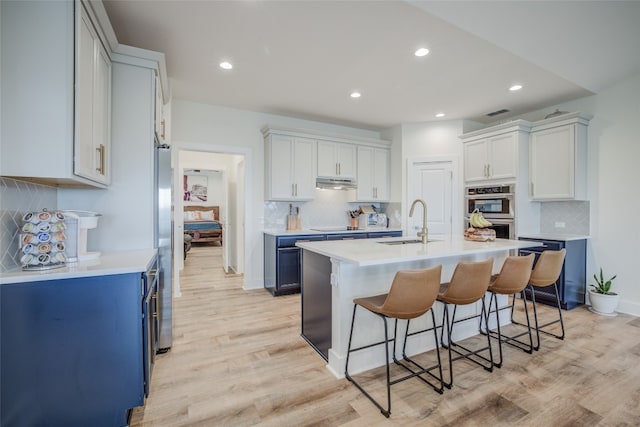 kitchen with appliances with stainless steel finishes, a kitchen island with sink, light hardwood / wood-style flooring, and white cabinets