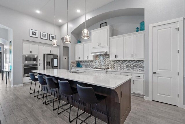 kitchen featuring a kitchen island with sink, light wood-type flooring, tasteful backsplash, stainless steel appliances, and white cabinets