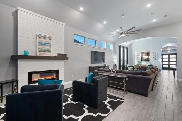 living room featuring ceiling fan, a fireplace, light hardwood / wood-style floors, and a towering ceiling