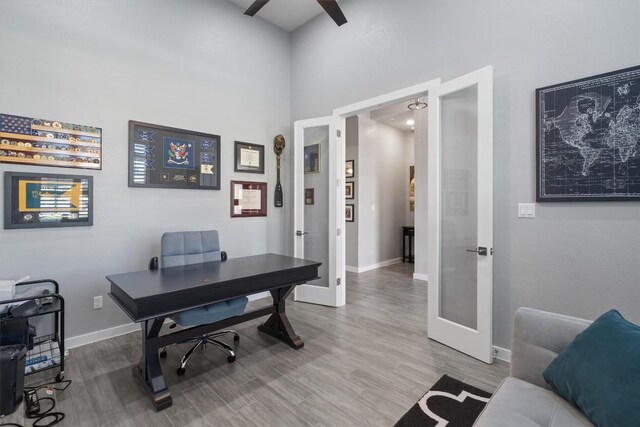 home office featuring a high ceiling, ceiling fan, hardwood / wood-style flooring, and french doors