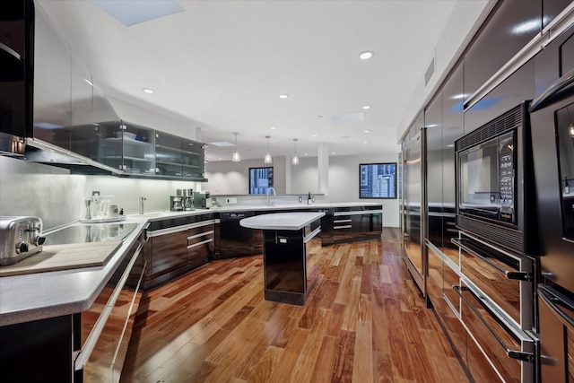 kitchen featuring a center island, black appliances, decorative light fixtures, light wood-type flooring, and a breakfast bar area