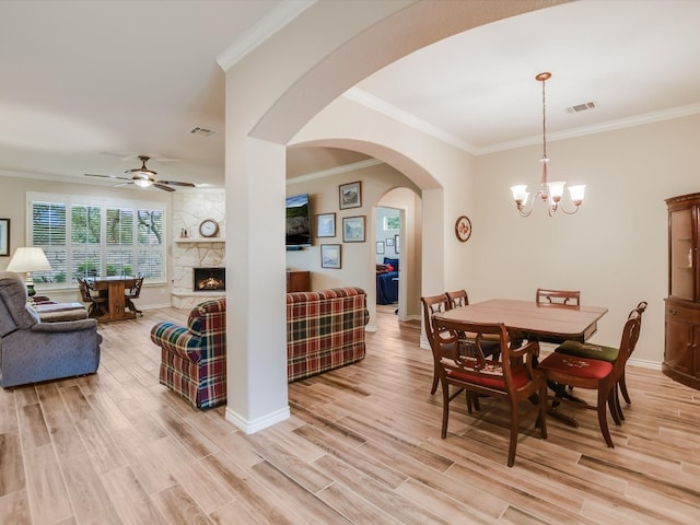 dining area featuring a fireplace, ceiling fan with notable chandelier, crown molding, and light hardwood / wood-style flooring