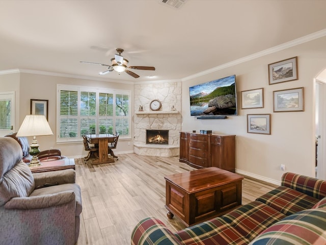 living room with ceiling fan, a stone fireplace, light hardwood / wood-style flooring, and crown molding