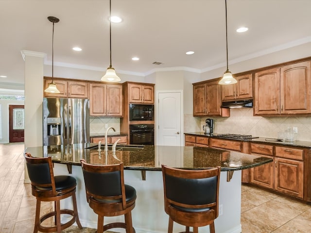 kitchen with hanging light fixtures, an island with sink, black appliances, and dark stone countertops