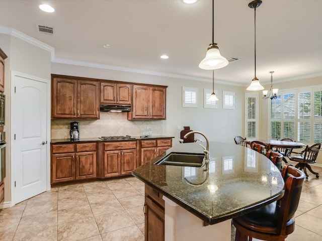 kitchen with a center island with sink, crown molding, sink, and dark stone counters