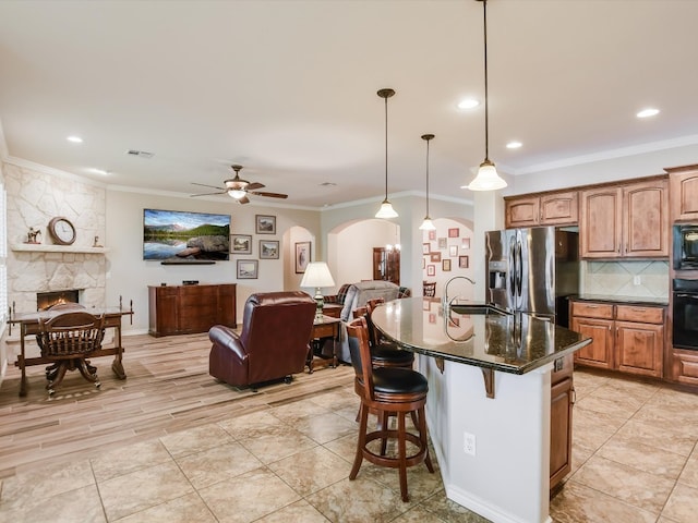 kitchen with ceiling fan, pendant lighting, dark stone counters, a center island with sink, and black appliances