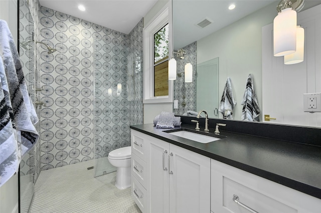 bathroom with toilet, vanity, tile patterned floors, and tiled shower