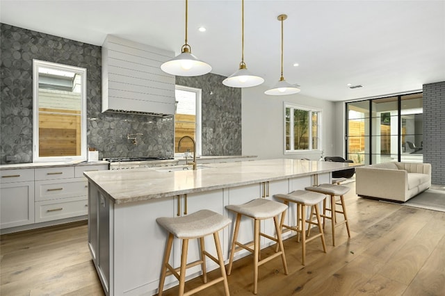 kitchen featuring a sink, open floor plan, light wood-type flooring, light stone countertops, and tasteful backsplash