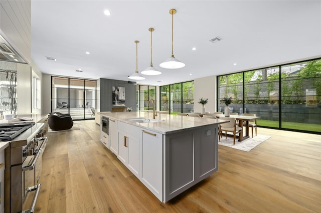 kitchen with white cabinets, an island with sink, sink, hanging light fixtures, and light stone counters