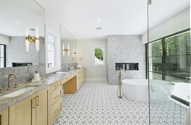 bathroom with double vanity, visible vents, a soaking tub, a fireplace, and a sink