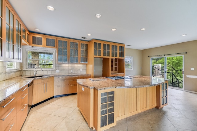 kitchen with sink, plenty of natural light, a kitchen island, and light stone countertops