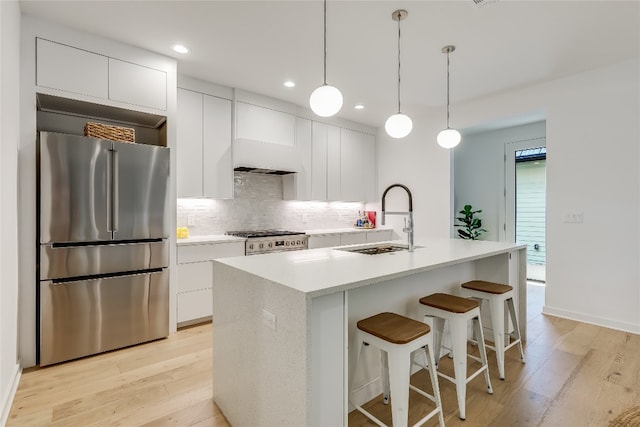 kitchen featuring stainless steel appliances, a center island with sink, light wood-type flooring, sink, and white cabinetry