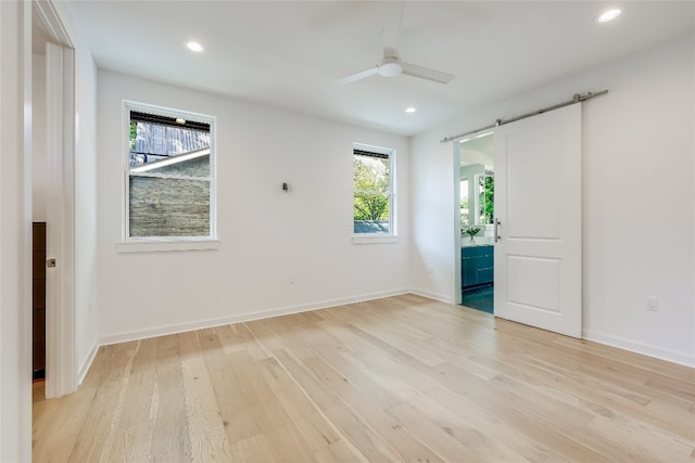 unfurnished bedroom with a barn door, multiple windows, light hardwood / wood-style flooring, and ceiling fan