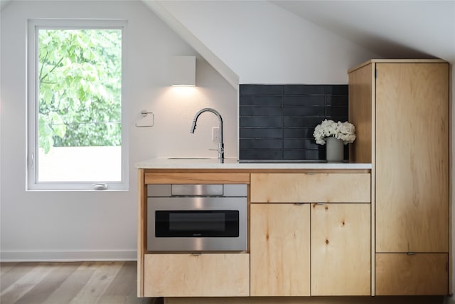 kitchen with light brown cabinets, sink, oven, and light wood-type flooring