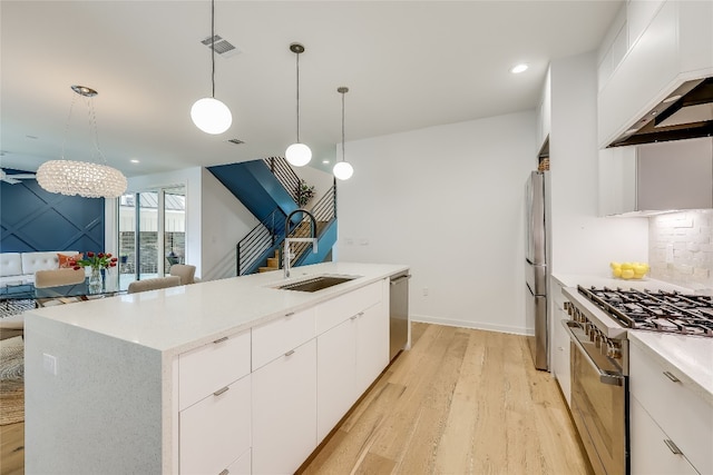 kitchen featuring decorative light fixtures, light hardwood / wood-style floors, stainless steel appliances, tasteful backsplash, and a kitchen island with sink