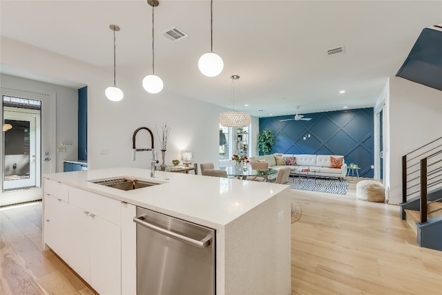 kitchen featuring light wood-type flooring, stainless steel dishwasher, an island with sink, decorative light fixtures, and sink