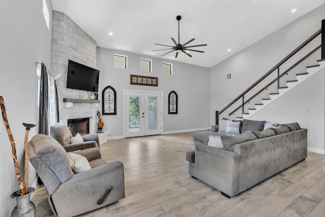 living room with ceiling fan, light hardwood / wood-style flooring, a fireplace, a high ceiling, and french doors