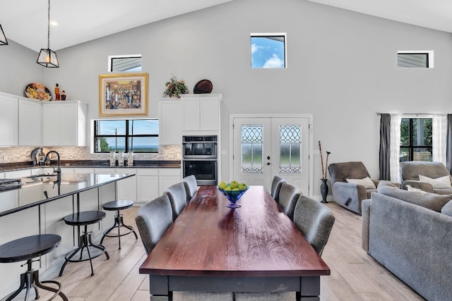 dining room featuring french doors, light hardwood / wood-style flooring, a wealth of natural light, and high vaulted ceiling