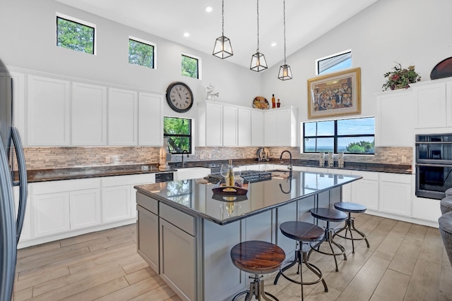 kitchen with backsplash, a wealth of natural light, white cabinets, and a kitchen island with sink