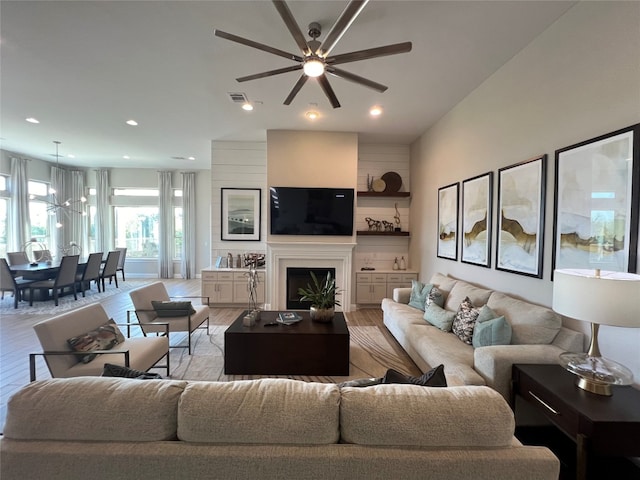 living room featuring ceiling fan, a large fireplace, and light wood-type flooring