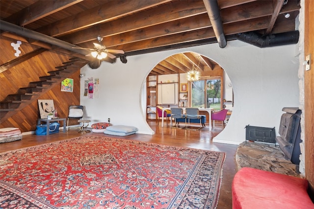 living room with ceiling fan, beamed ceiling, a wood stove, and wooden walls