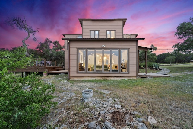 back house at dusk with a wooden deck and a lawn