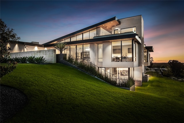 back house at dusk featuring a yard and a balcony