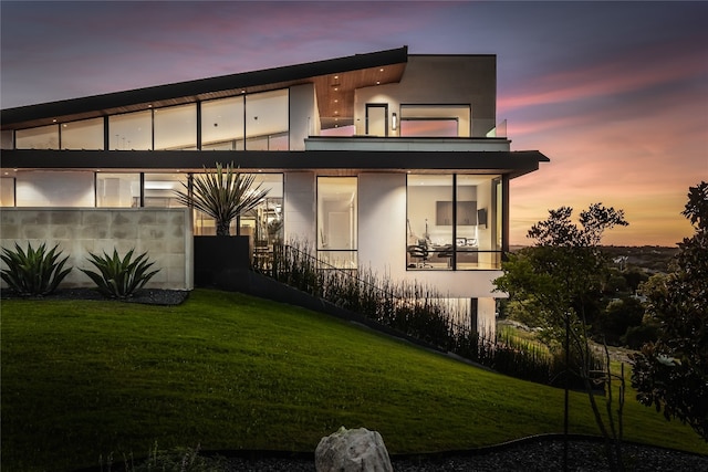 back house at dusk featuring a lawn