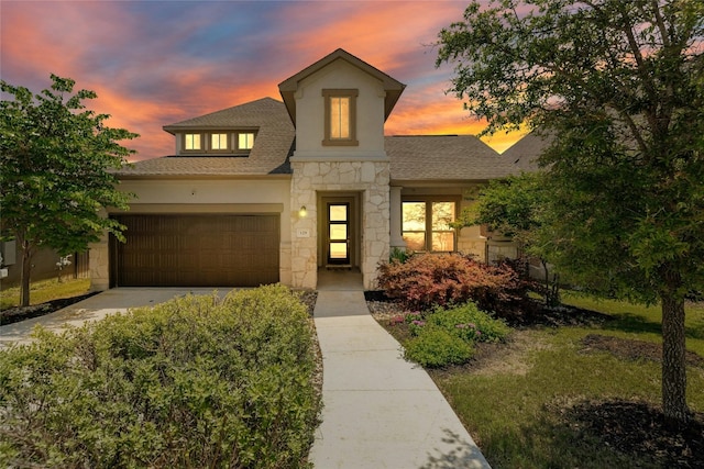 view of front of property featuring an attached garage, a shingled roof, stone siding, driveway, and stucco siding