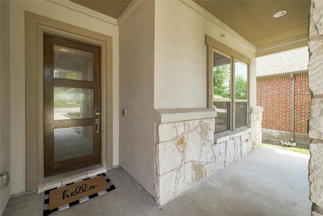 property entrance featuring covered porch, stone siding, and stucco siding