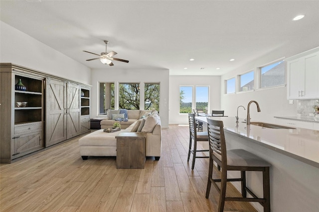 living room with a healthy amount of sunlight, sink, ceiling fan, and light hardwood / wood-style floors