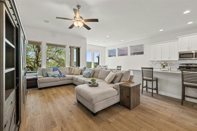 living room with ceiling fan, sink, and light hardwood / wood-style flooring