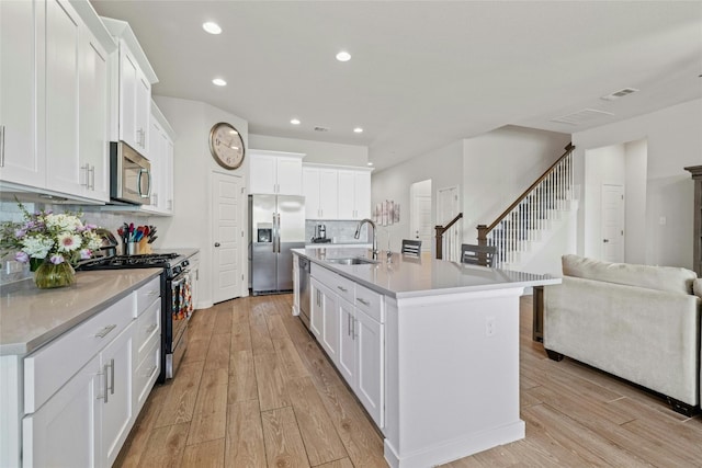 kitchen with decorative backsplash, stainless steel appliances, sink, a center island with sink, and white cabinetry