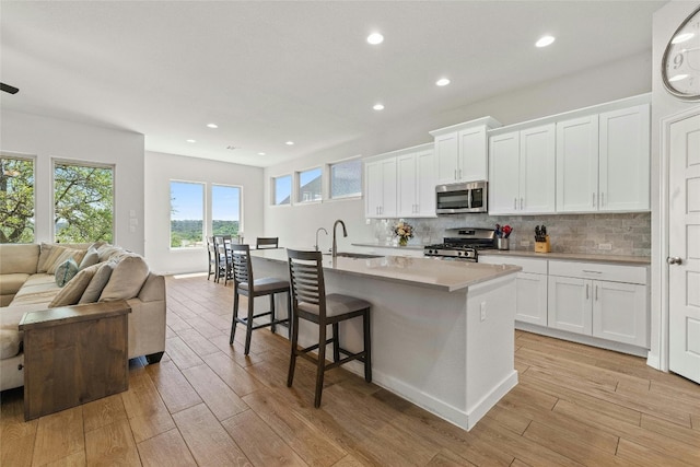 kitchen featuring light wood finished floors, stainless steel appliances, backsplash, open floor plan, and a sink