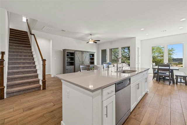 kitchen with stainless steel dishwasher, white cabinets, sink, and an island with sink