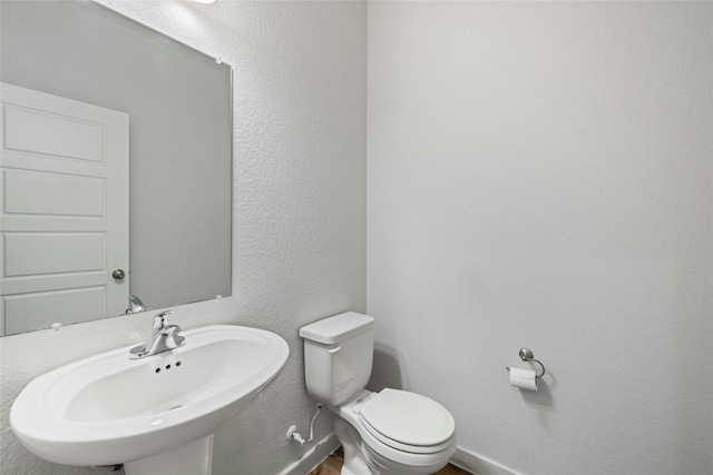 half bath with a textured wall, a sink, toilet, and baseboards