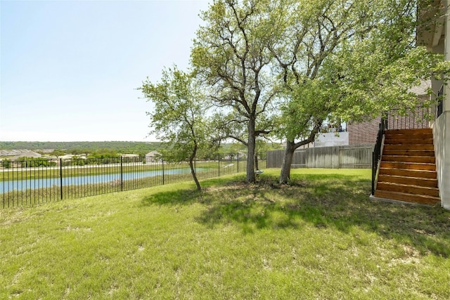 view of yard with a water view, fence, and stairs