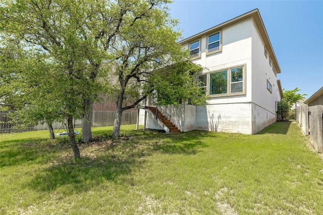 view of property exterior with stucco siding, a fenced backyard, stairway, and a yard