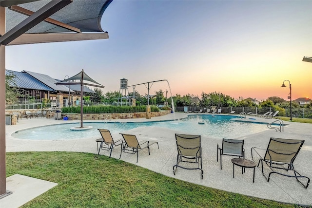 pool at dusk with a patio, a lawn, fence, and a community pool