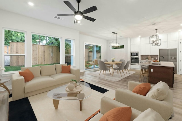 living room with sink, ceiling fan with notable chandelier, and light hardwood / wood-style flooring