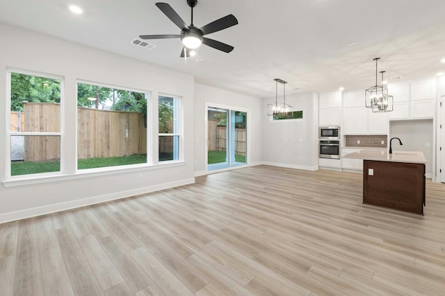 kitchen featuring built in microwave, hanging light fixtures, oven, a kitchen island with sink, and white cabinets