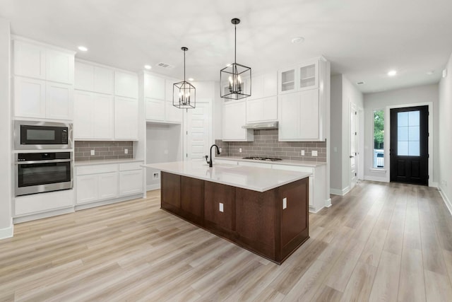 kitchen with appliances with stainless steel finishes, sink, white cabinets, light hardwood / wood-style floors, and a center island with sink