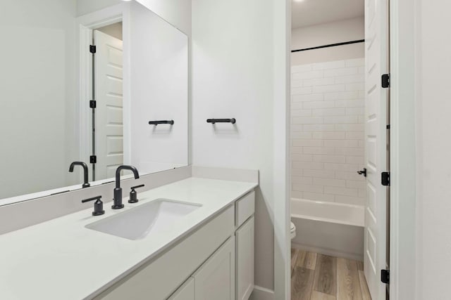 full bathroom featuring hardwood / wood-style flooring, tiled shower / bath, vanity, and toilet