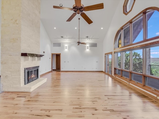 unfurnished living room with a stone fireplace, light hardwood / wood-style flooring, high vaulted ceiling, and ceiling fan