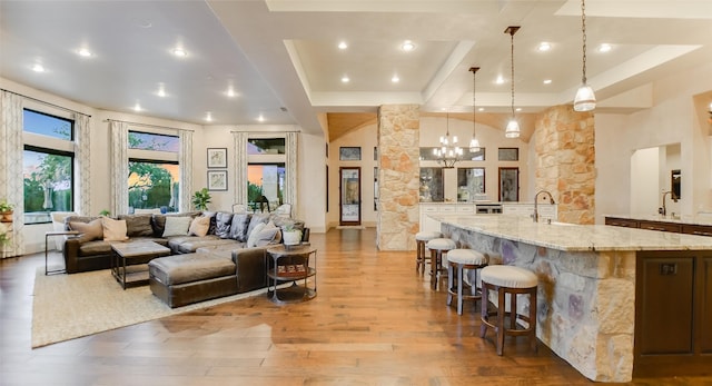 living room with a raised ceiling, light hardwood / wood-style flooring, sink, and a chandelier