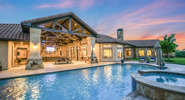 pool at dusk with an in ground hot tub and a patio area