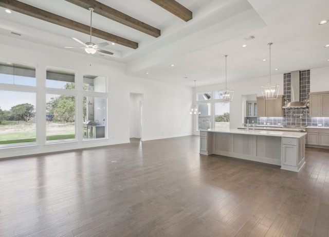 kitchen with ceiling fan with notable chandelier, wall chimney exhaust hood, dark hardwood / wood-style flooring, and a spacious island