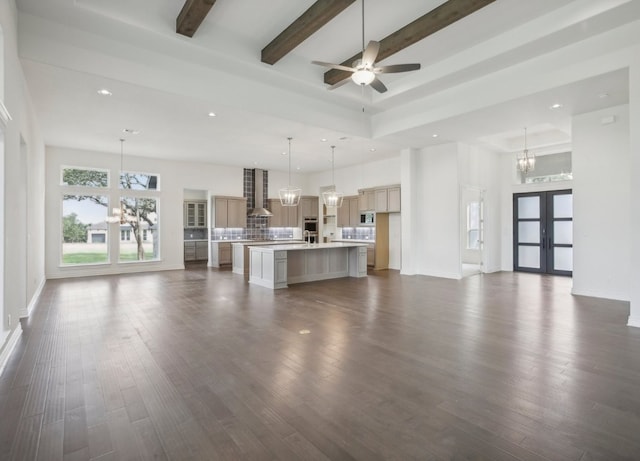 unfurnished living room featuring ceiling fan with notable chandelier, beam ceiling, and dark wood-type flooring