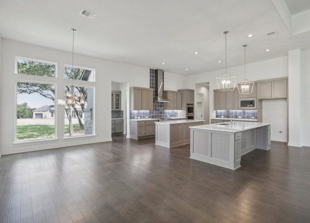 kitchen with hanging light fixtures, a kitchen island with sink, wall chimney exhaust hood, and a wealth of natural light