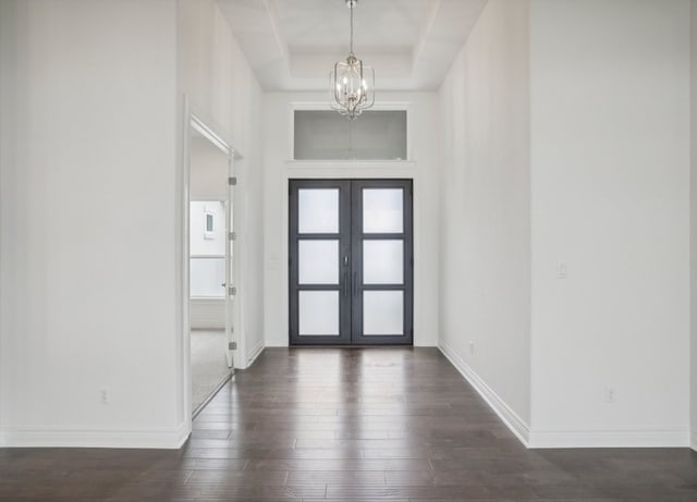 foyer entrance with french doors, an inviting chandelier, a tray ceiling, and dark hardwood / wood-style floors